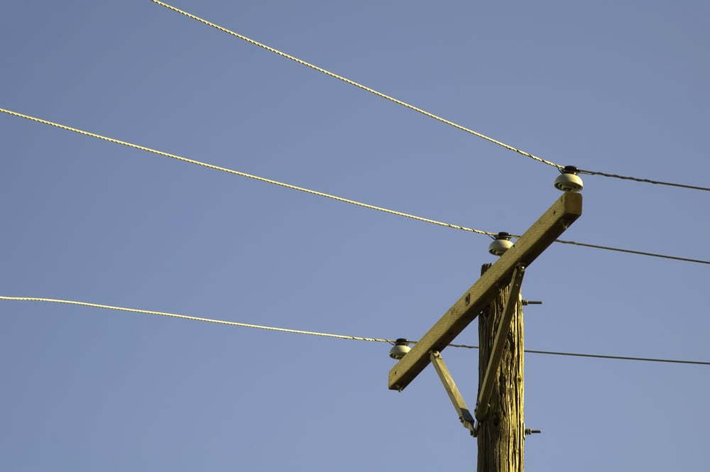 Top of utility pole with three power lines against blue sky at sunset